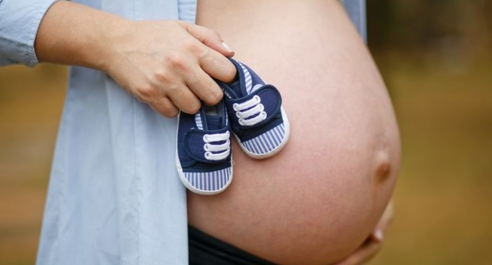 Vientre materno adornado con un zapatitos de bebé.